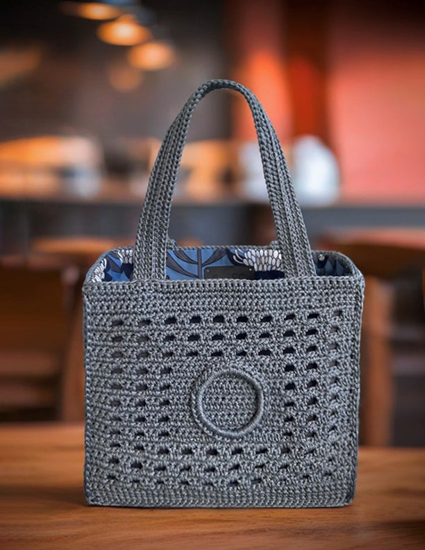 Large crochet square market bag standing on the wooden table at a cafe